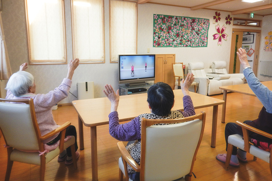 グループホームおきだて内で映像を見ながら体操をしている入居者